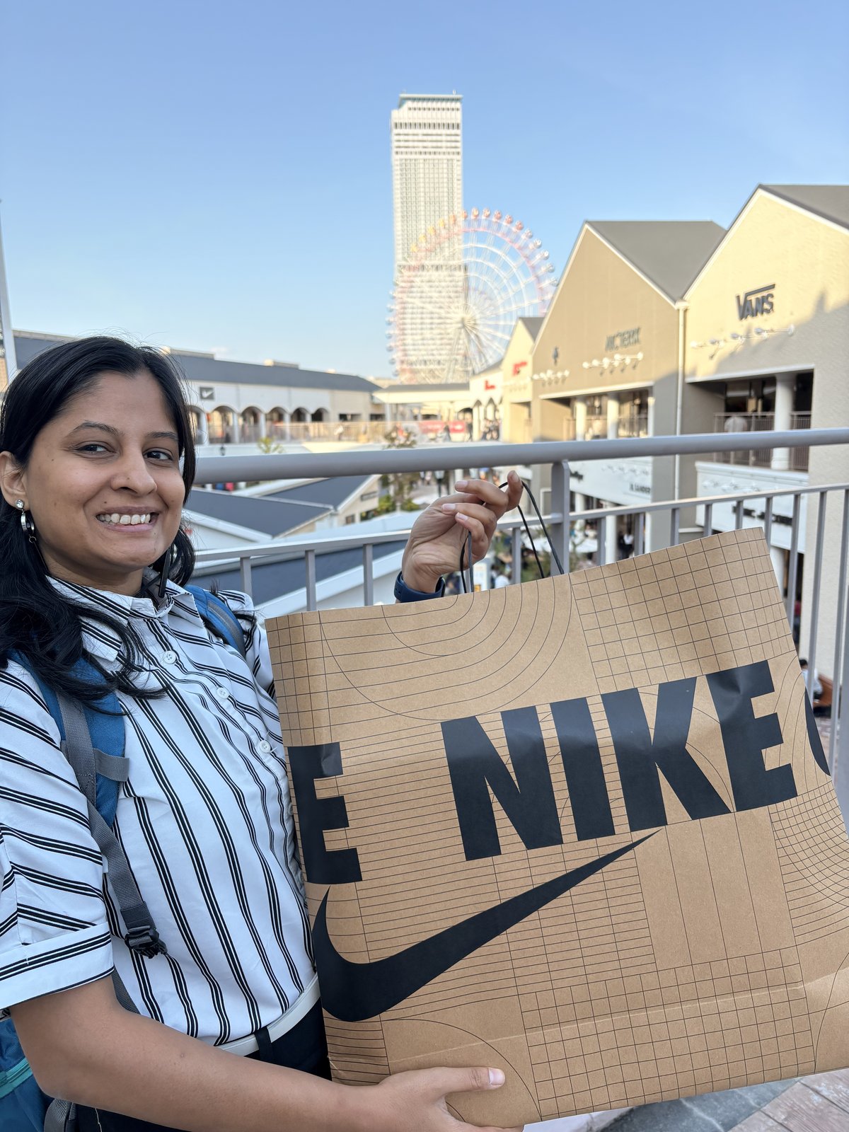 Holding a Nike shopping bag at Rinku Premium Outlet, Ferris wheel in the background