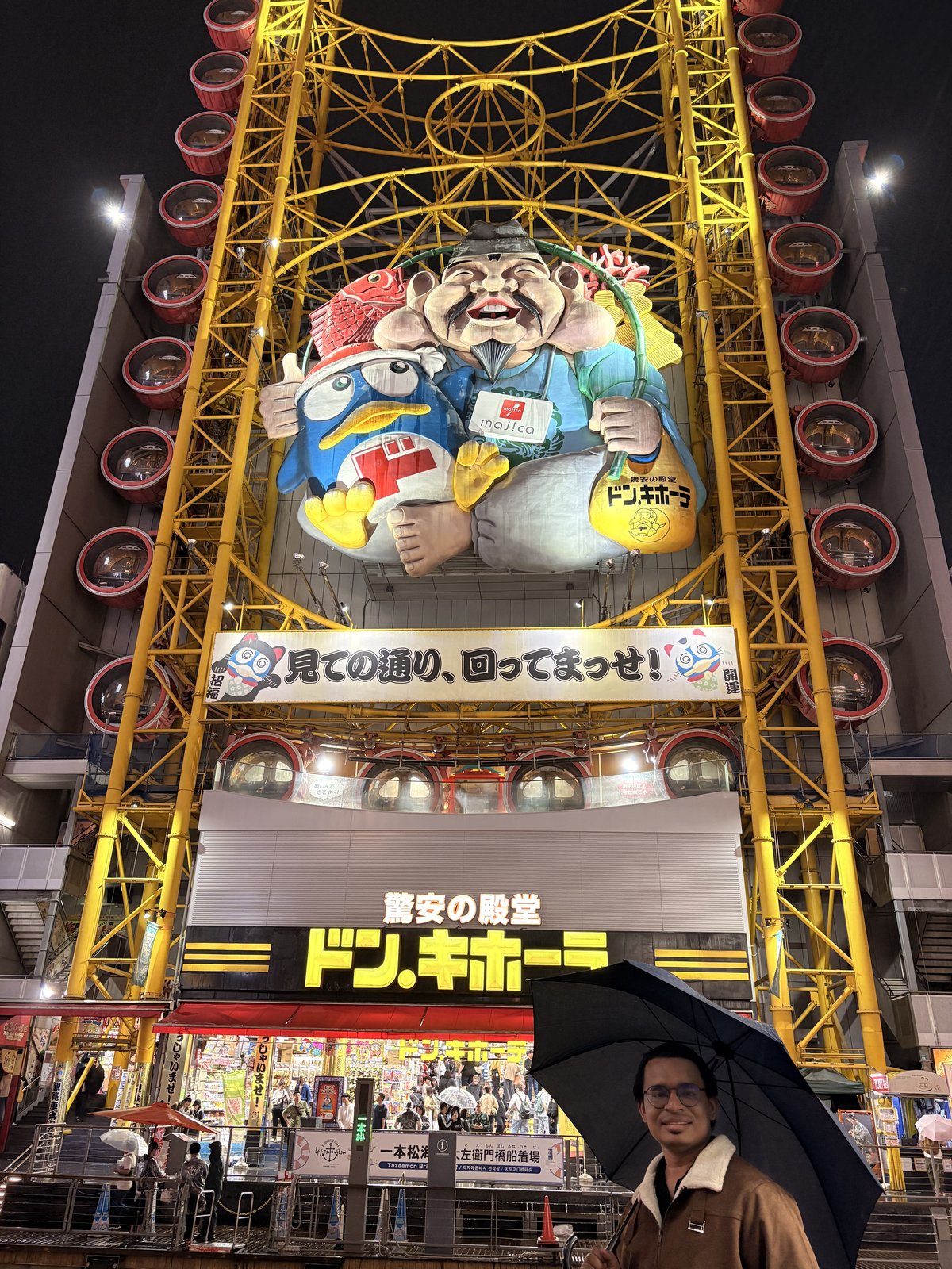 Don Quijote Dotonbori with its yellow Ferris wheel and giant mascot at night in the rain